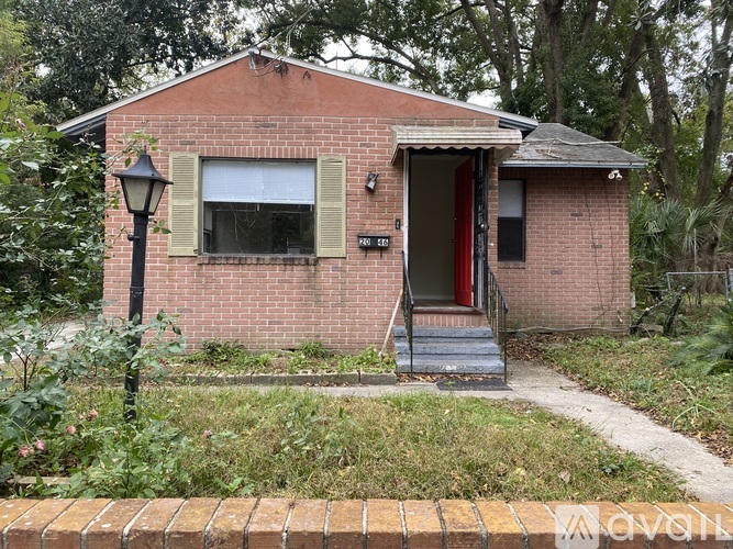 A small red brick house with a white door and a window with green shutters.