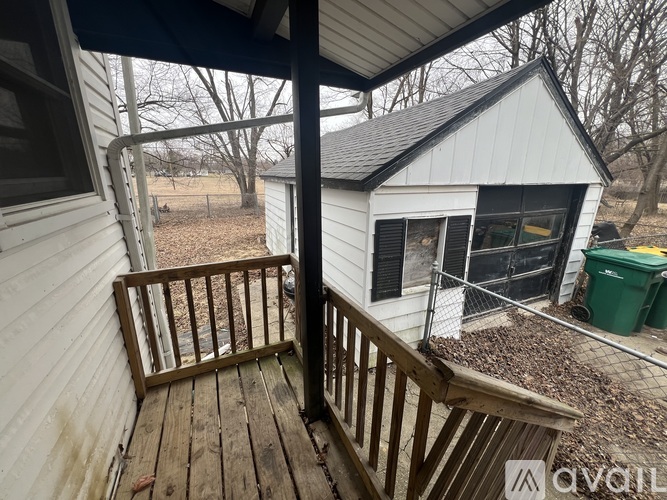 A small white house with a porch and a green trash can in the yard.