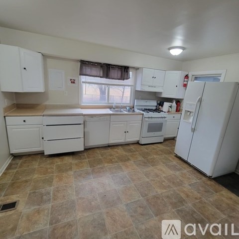 A kitchen with white cabinets and appliances, a window with a view, and a tiled floor.