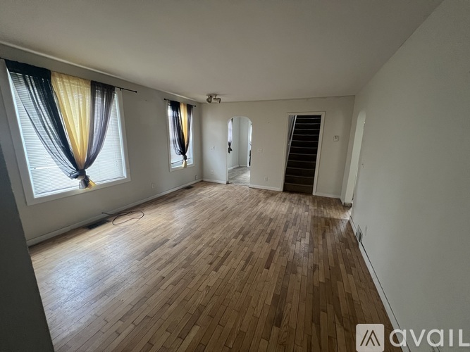 A room with wooden flooring and two windows with curtains.