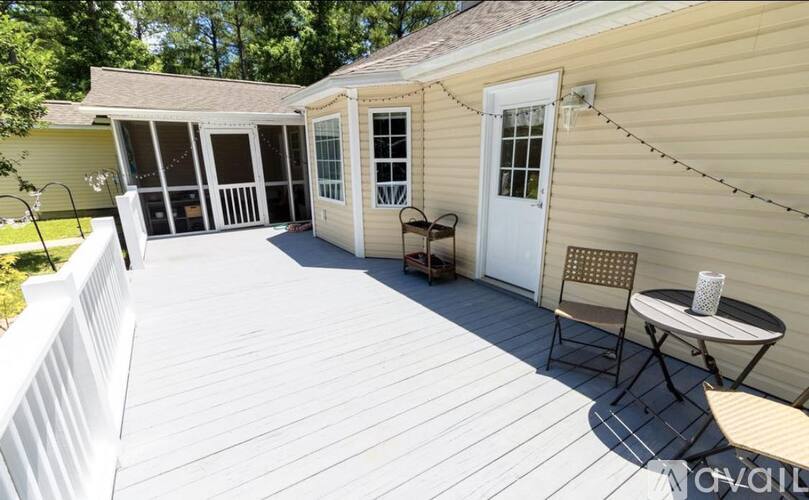 A deck with a white railing, a table and chairs, and a small building with windows.