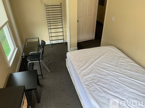 A bedroom with a bed, desk, chair, and a window.