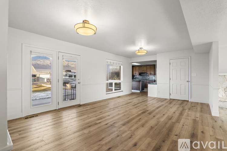 A spacious room with wooden floors and white walls, featuring a large window with a view of a snowy landscape.