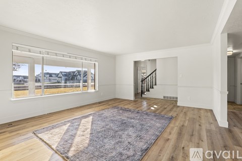 A spacious living room with a large rug and a staircase in the background.