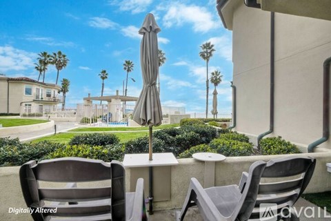 A patio with chairs and an umbrella overlooking a pool and palm trees.