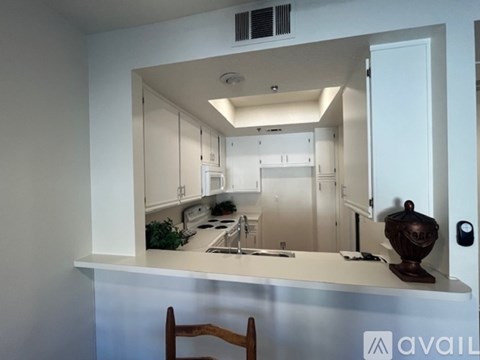 A kitchen with white cabinets and a white countertop with a wooden chair in front of it.