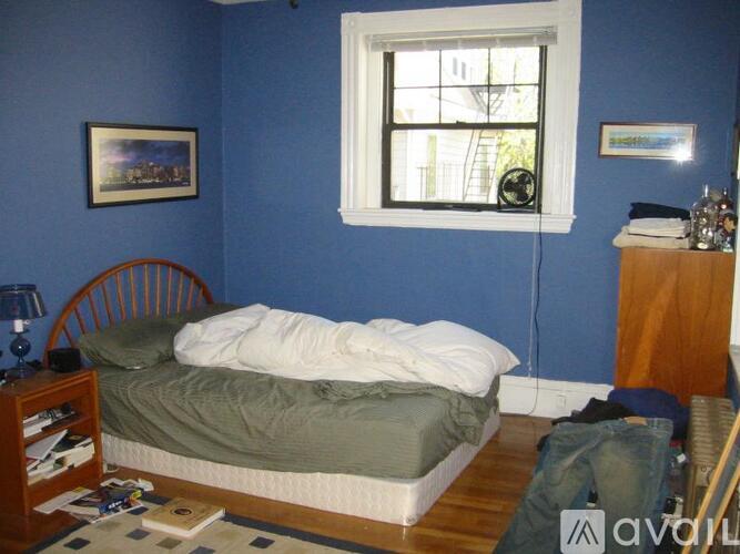 A bedroom with a bed, a window, a nightstand, and a bookshelf.