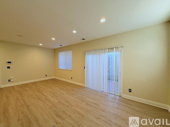 A spacious room with wooden flooring and a window with white curtains.