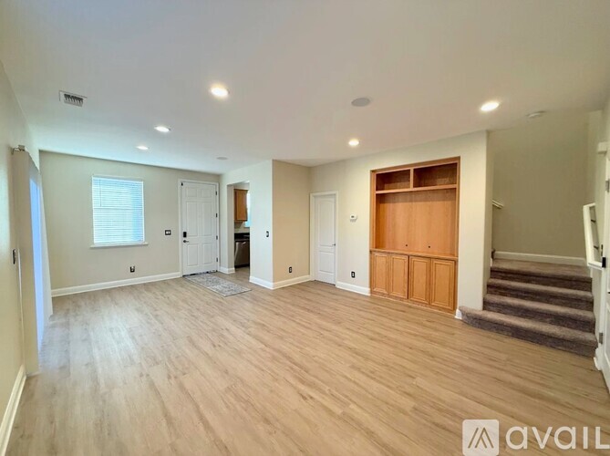A spacious room with wooden flooring and a staircase on the right side.