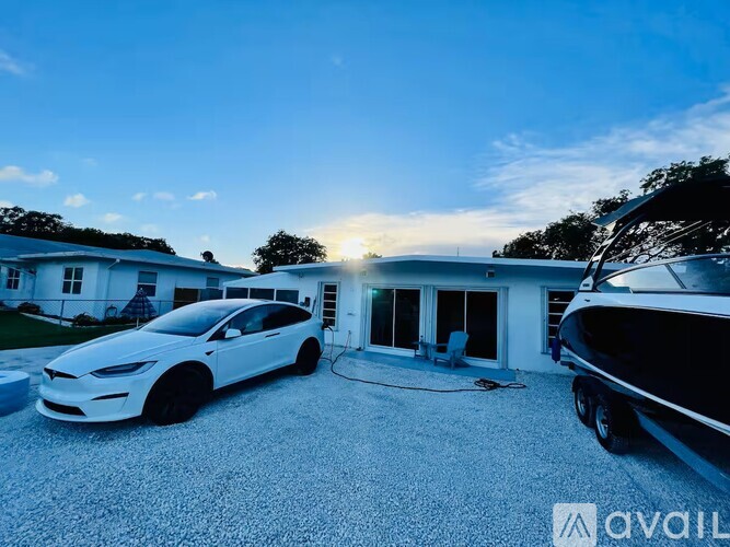 A white car is parked in front of a house with a boat in the driveway.