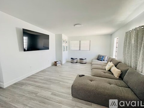 A living room with a grey couch and a flat screen TV mounted on the wall.