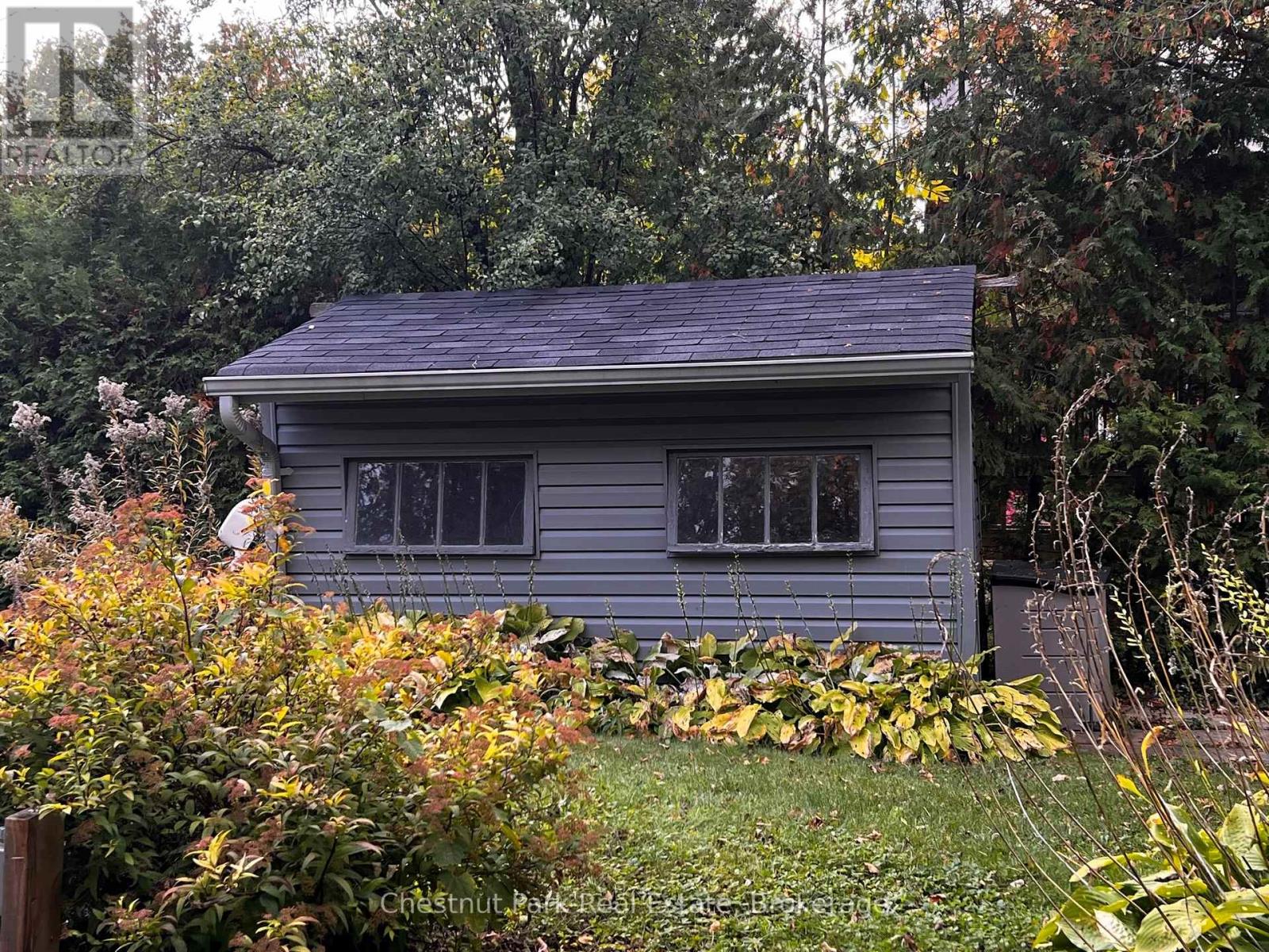 A small house with a grey roof surrounded by greenery and trees.