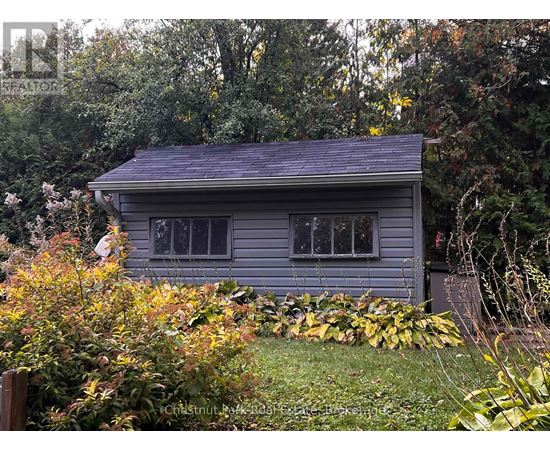 A small house with a grey roof surrounded by greenery and trees.