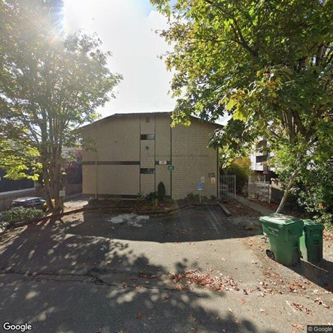 A street view of a building with a green trash bin in front.
