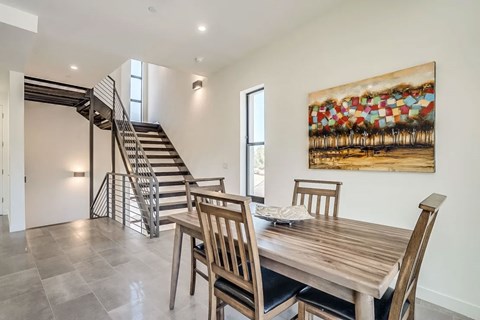 A dining room with a wooden table and chairs and a painting on the wall.