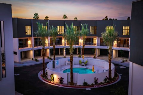 A pool surrounded by palm trees and a building in the background.