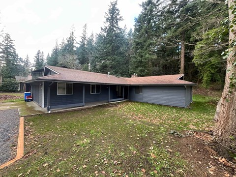 A house with a grey roof and a grey garage door is surrounded by trees.
