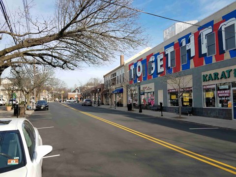 A street with a white car parked on the side and a building with the word "TOGETHER" on it.