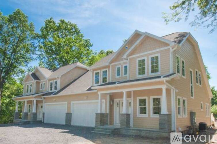 A large, two-story house with a garage is surrounded by trees.