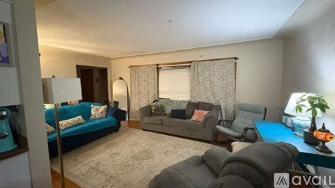 A living room with a blue couch, a grey couch, a grey armchair, and a table with a plant on it.