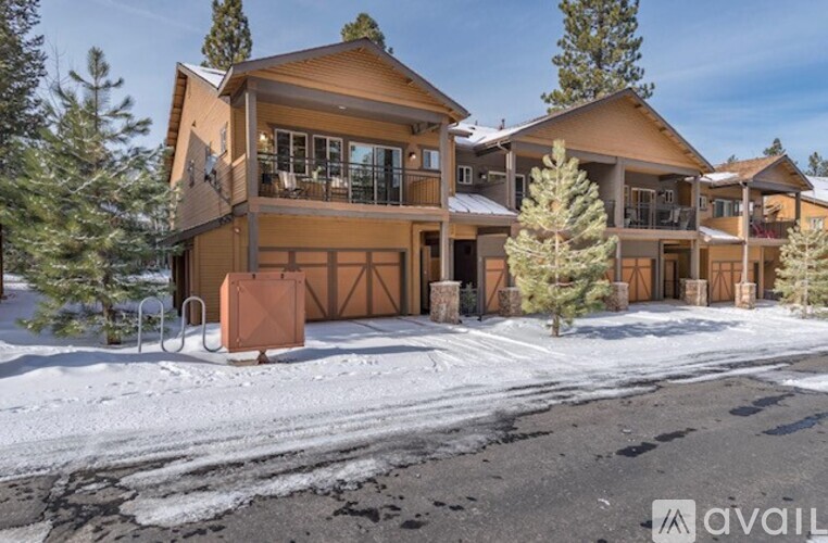 A large, modern house with a brown exterior and a snow-covered driveway in front.
