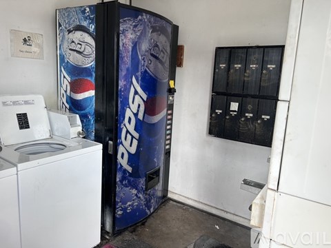 A Pepsi machine is in front of a wall with a white washing machine behind it.