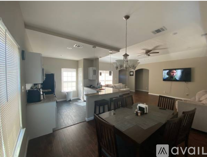A modern dining room with a dark wood table and chairs, a television, and a kitchen area in the background.