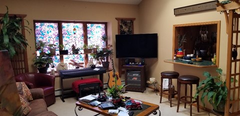 A living room with a stained glass window, a piano, a TV, and a bar area.