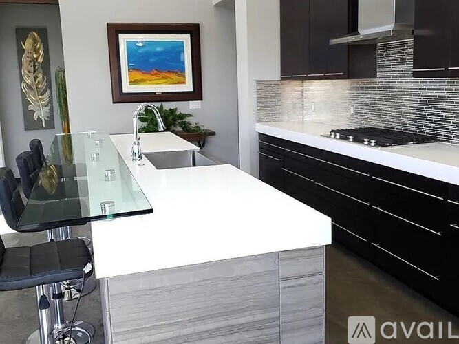 A modern kitchen with a glass table and black chairs.
