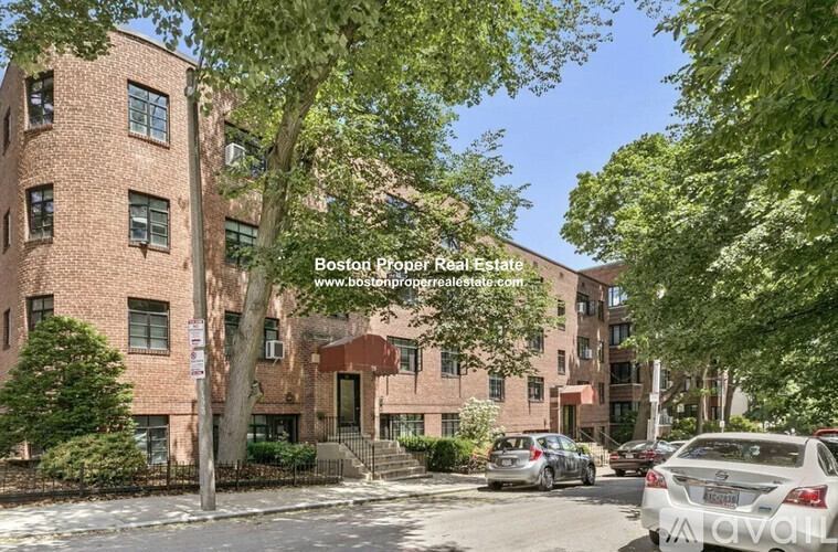 A street view of a residential area with cars parked on the side of the road and apartment buildings in the background.