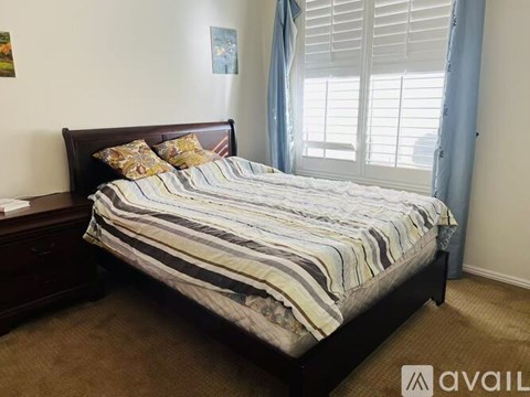 A bedroom with a bed, nightstand, and window with blinds.