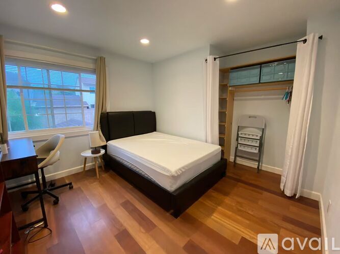 A white door is on the left of a room with a white wall and a white bed.