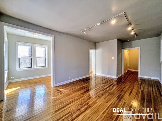 A spacious room with wooden floors and a window on the left side.