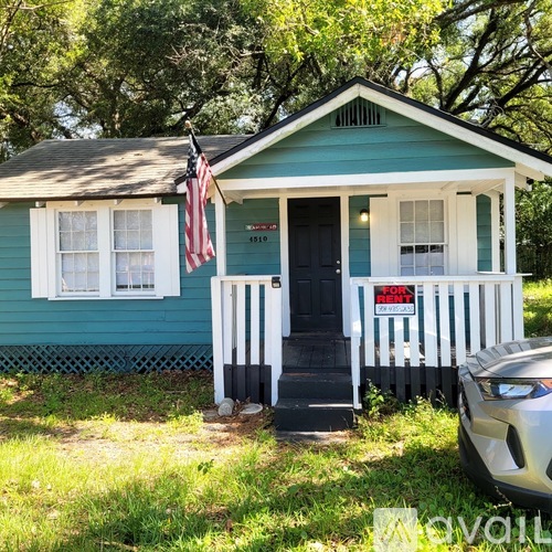 A small blue house with a black door and a "For Sale" sign in front.