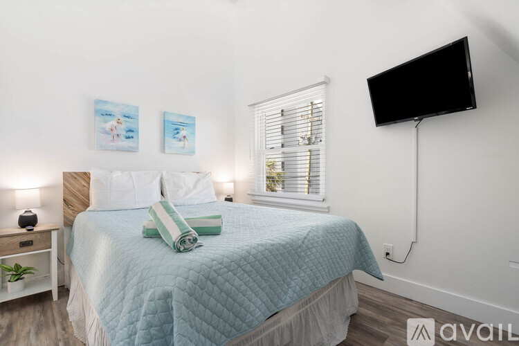 A bedroom with a bed, a window with blinds, a nightstand with a lamp, and two pictures on the wall.