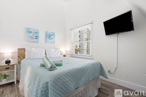 A bedroom with a bed, a window with blinds, a nightstand with a lamp, and two pictures on the wall.