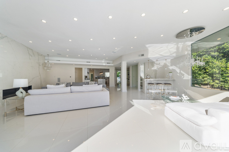 A modern, white bedroom with a large bed and a view of the outdoors.