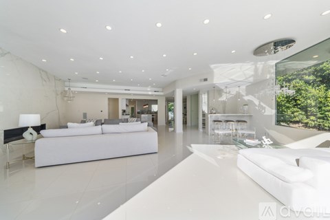 A modern, white bedroom with a large bed and a view of the outdoors.
