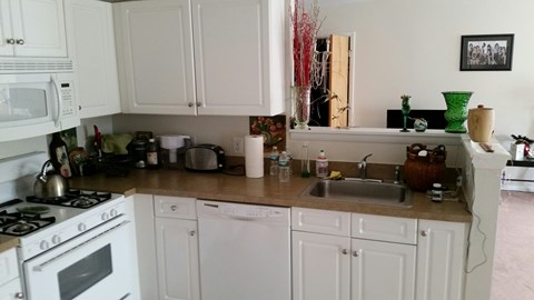 A white kitchen with a stove, sink, and cabinets.