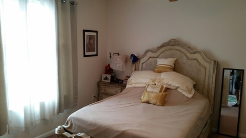 A bedroom with a large bed and a window with curtains.