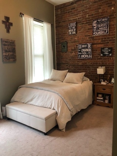 A bedroom with a brick wall and a bed with a white comforter.
