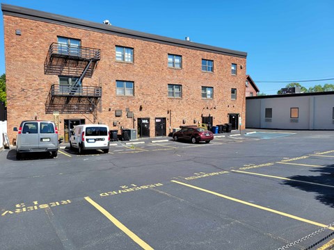 A parking lot with a red car parked in front of a brick building.