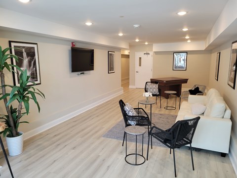 A living room with a white couch, a black chair, and a television on the wall.