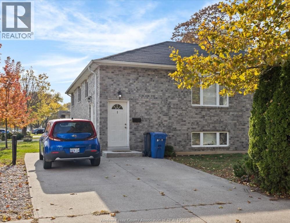 A blue car is parked in front of a grey house.