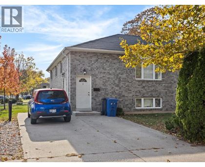 A blue car is parked in front of a grey house.