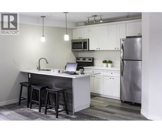 A kitchen with a bar stool and a laptop on the counter.