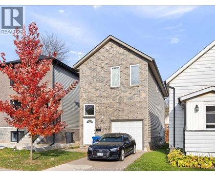 A black car is parked in front of a brick house.