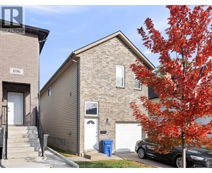 A tree with red leaves is in front of a house with a car parked in front of it.