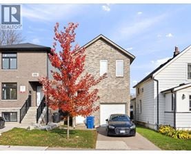 A tree with red leaves is in front of a brick house with a car parked in front of it.