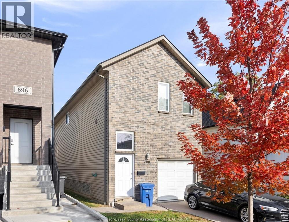 A tree with red leaves is in front of a house with a car parked in front of it.